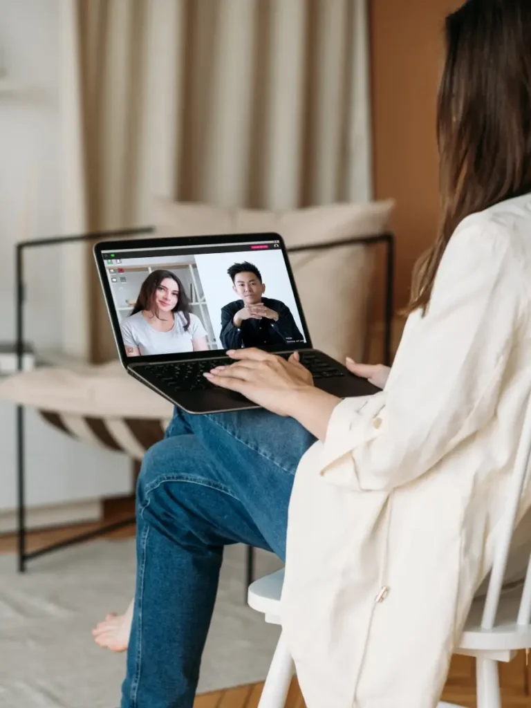 Eine Person sitzt und führt ein Videogespräch auf einem Laptop mit zwei anderen Personen.